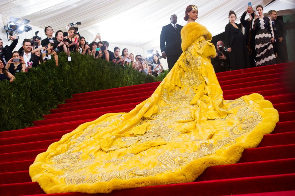 Rihanna poses on the red carpet of the Met Gala in 2015, dressed in a sweeping yellow robe.