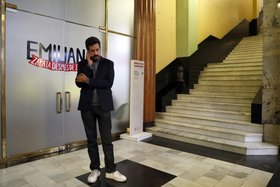 Mexican artist Fabian Chairez speaks on his mobile phone at the Fine Arts Palace where it is exhibited his painting showing Mexican Revolution hero Emiliano Zapata straddling on a horse nude, wearing high heels and a pink, broad-brimmed, in Mexico City, Wednesday, Dec. 11, 2019. Mexico President Andres Manuel Lopez Obrador says he'll ask his culture minister to mediate a dispute over an effeminate painting of Zapata. (AP Photo/Marco Ugarte)