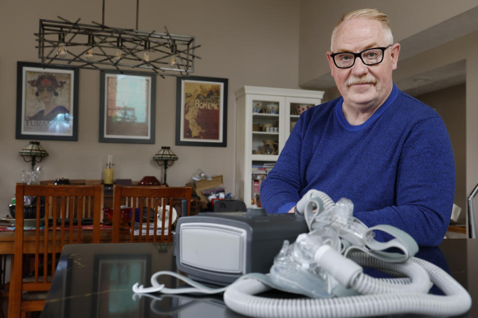 Jeffrey Reed, who experienced persistent sinus infections and two bouts of pneumonia while using a Philips CPAP machine, poses with the device at his home Thursday, Oct. 20, 2022, in Marysville, Ohio. The device is part of a massive global recall of breathing machines triggered by sound-dampening foam that can break down, releasing potentially harmful particles and chemicals. (AP Photo/Jay LaPrete)