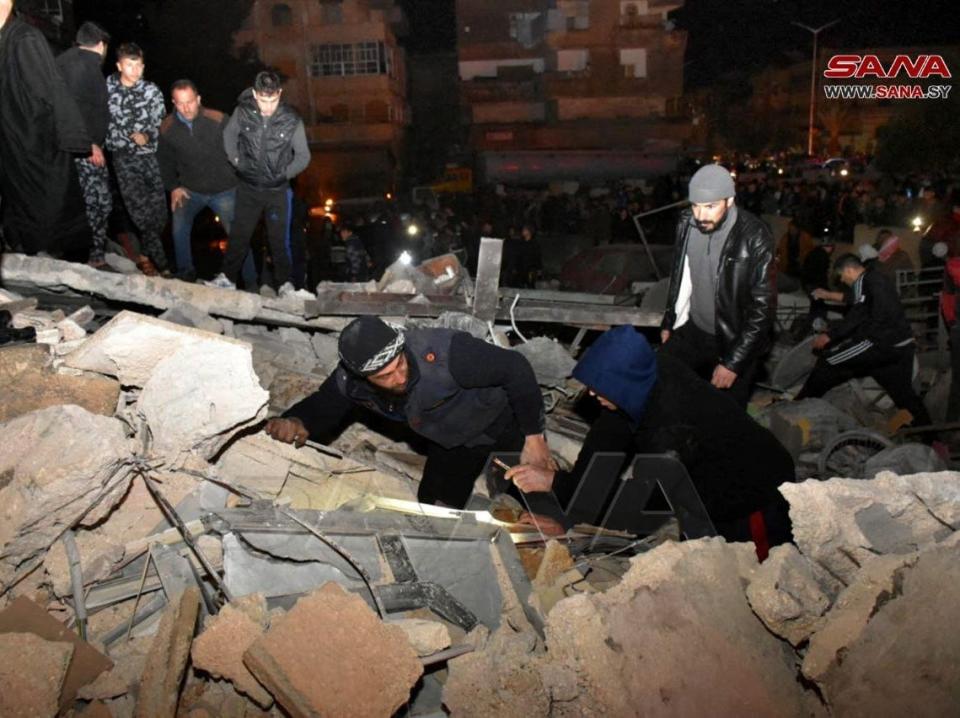 Men search under the rubble at the site of a collapsed building, following an earthquake, in Hama, Syria, in this handout released by SANA on February 6, 2023.