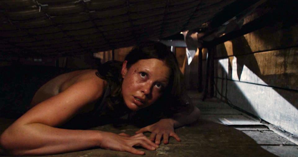 Mia Goth hiding under a bed.