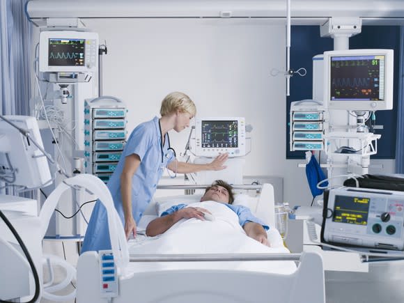 Hospital room with medical professional and patient surrounded by medical devices.