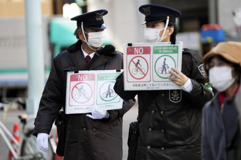 Security guards wearing protective masks to help curb the spread of the coronavirus walk with public notice signs saying in Japanese, "No bicycles allowed on the sidewalk," Monday, Jan. 31, 2022, in Tokyo. (AP Photo/Eugene Hoshiko)