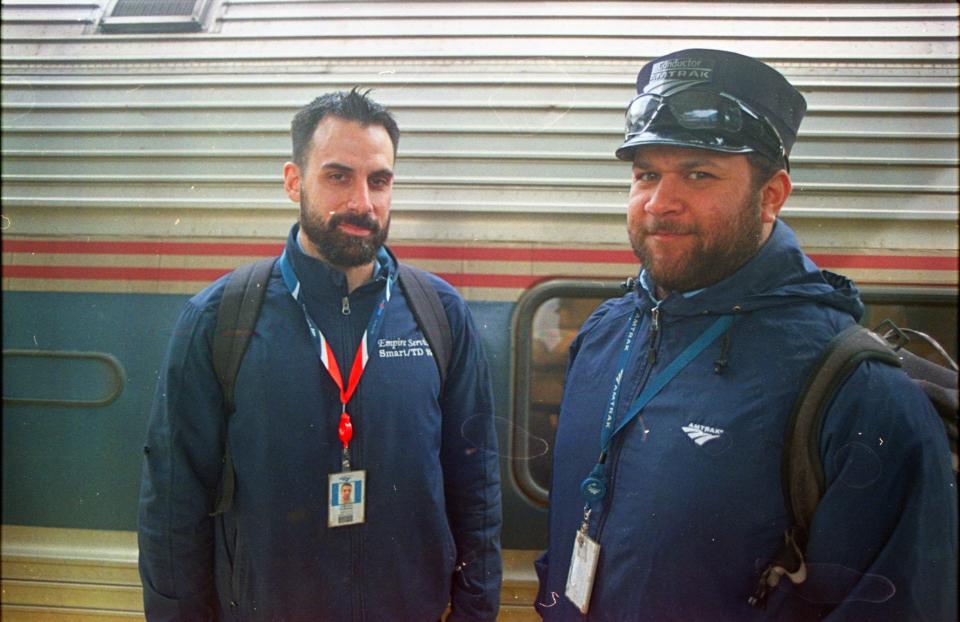 two amtrak employees in navy uniforms in front of train