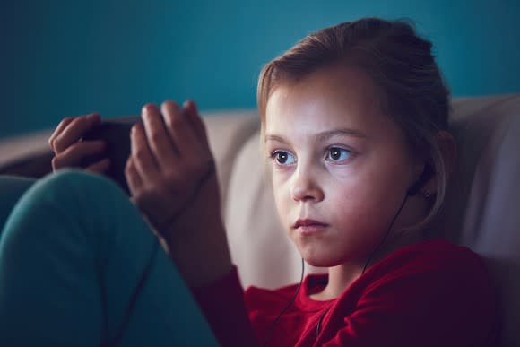 A young girl staring at a mobile phone.