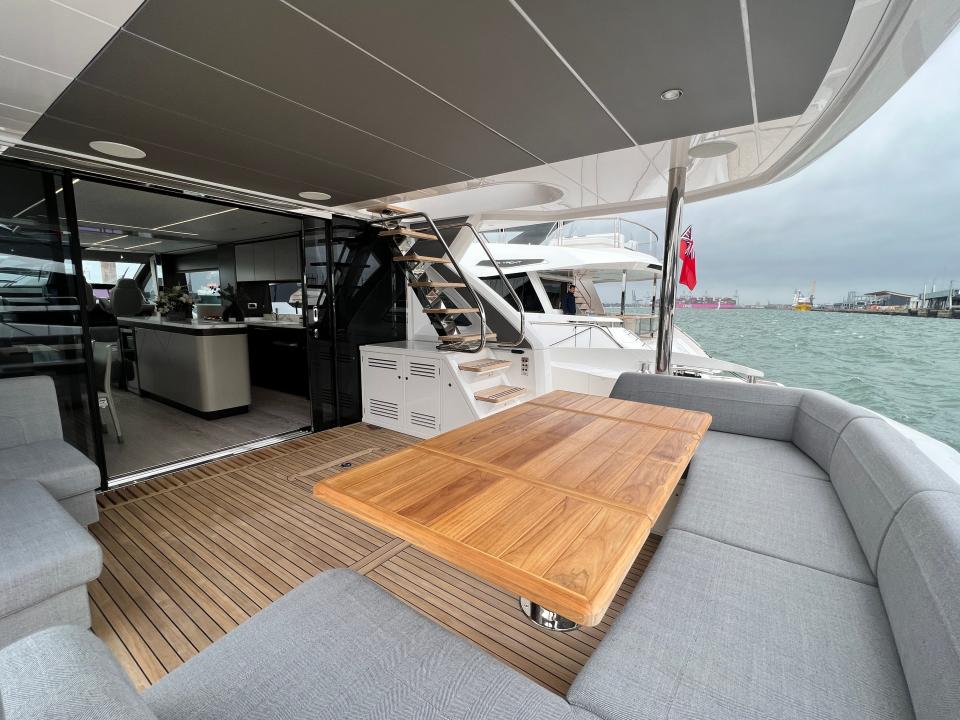 The outdoor seating area with grey seats and a wooden table at the stern of a Sunseeker 76 yacht