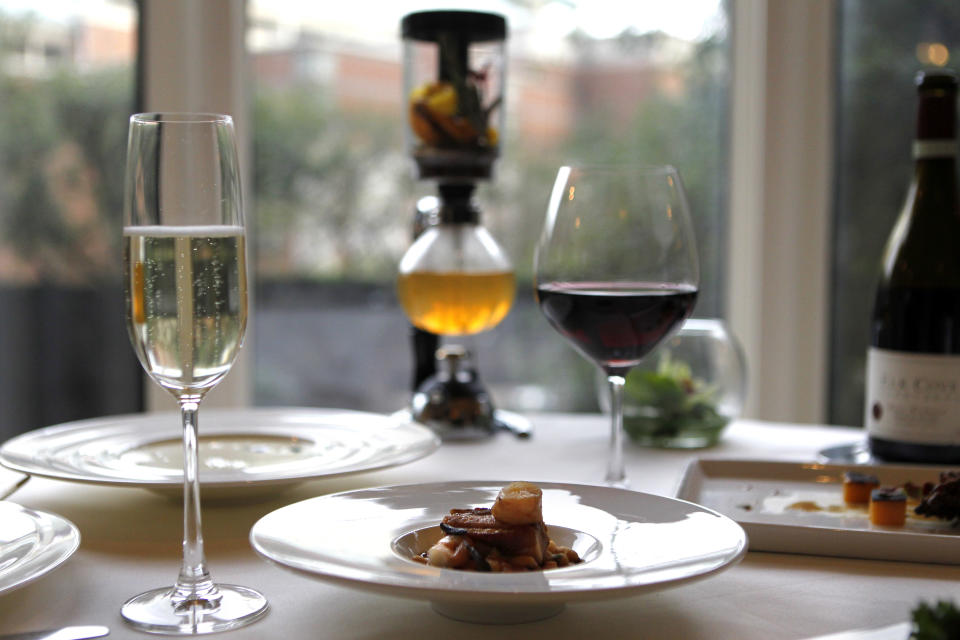 In this Dec. 7, 2012 photo, braised pork belly with gulf shrimp, white bean cassoulet, garlic jus and fried baby sage, by executive chef Kristin Butterworth, is seen with wine pairings and cafe brulot in a tea siphon, center rear, at the Grill Room of the Windsor Court Hotel in New Orleans. Roughly 50 restaurants in New Orleans are reviving an old Creole custom called reveillon, which stems from the old French tradition of eating a lavish meal after midnight Mass on Christmas Eve. (AP Photo/Gerald Herbert)