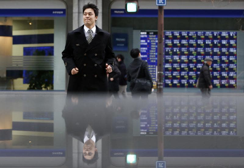 Pedestrians pass by an electronic board displaying stock prices, which are reflected in a polished stone surface, in Tokyo March 7, 2014. REUTERS/Yuya Shino