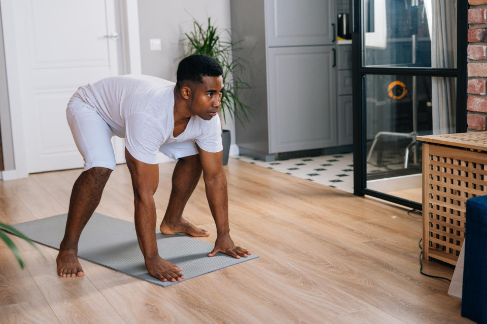  man practicing burpee exercise at home, doing push-ups and jumping on yoga mat at bright domestic room. Concept of sport training at home gym.