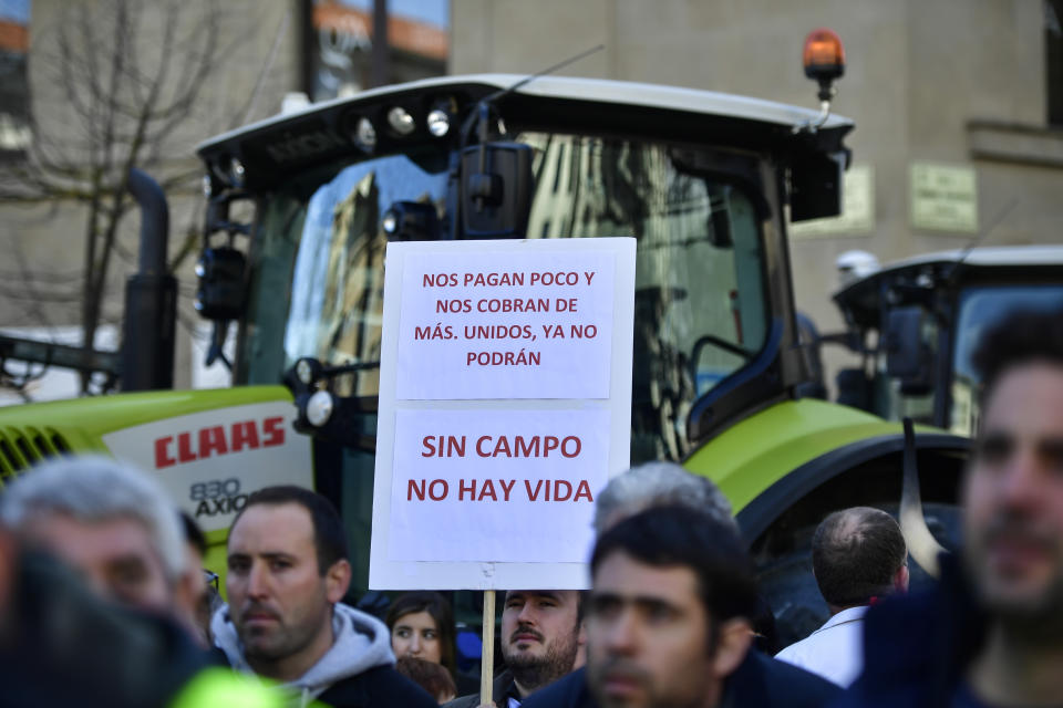 A man holds up a banner reading, ''They pay us little and they charge us more. If we are united they will can no longer. Without fields there is no life'' during a protest in Pamplona, northern Spain, Wednesday, Feb. 19, 2020. Farmers across Spain are taking part in mass protests over what they say are plummeting incomes for agricultural workers. (AP Photo/Alvaro Barrientos)
