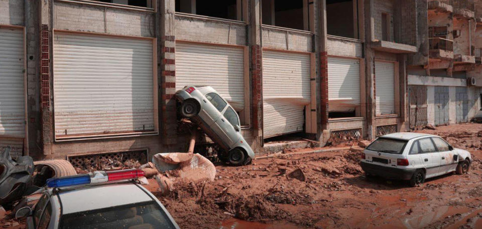 A car is tipped at a 45-degree angle on a mud-covered street.