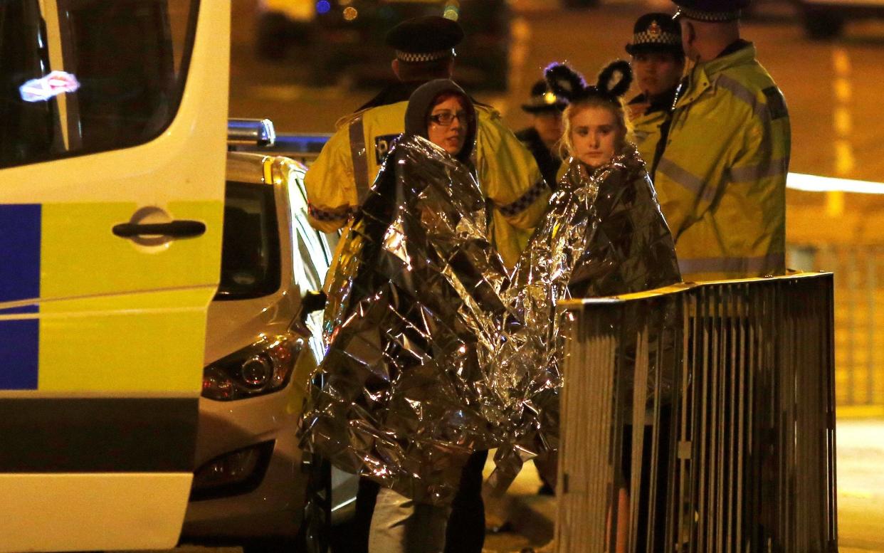 Two girls wrapped in thermal blankets stand near the Manchester Arena following the explosion - REUTERS