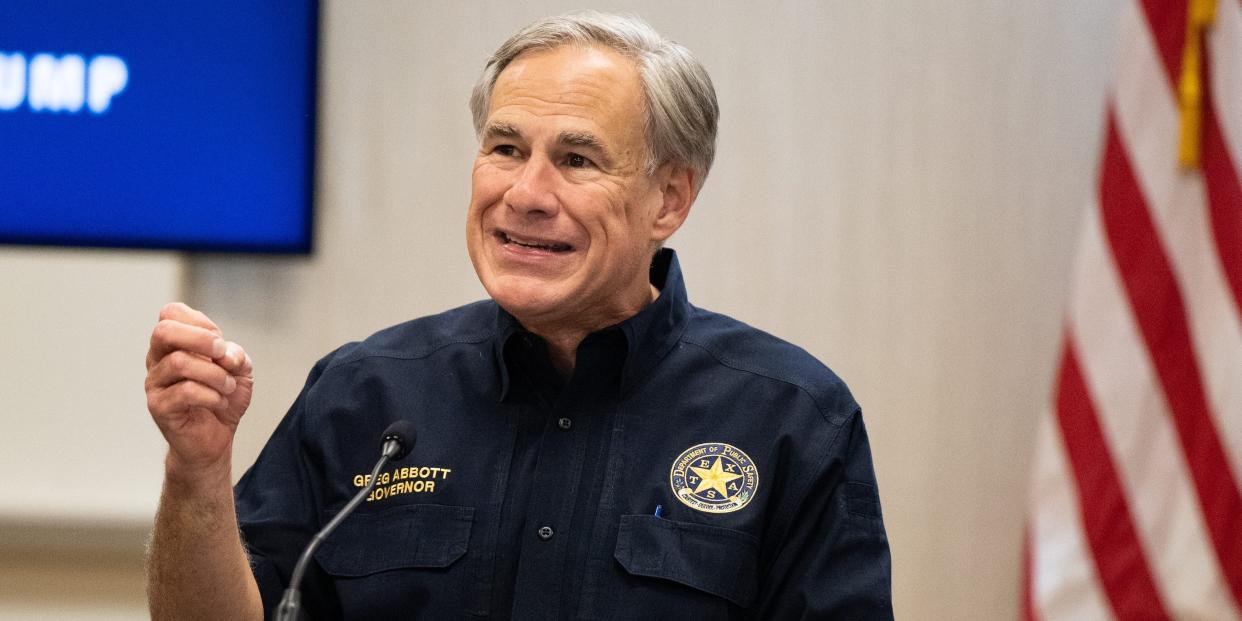 Greg abbott sits in front of a US flag