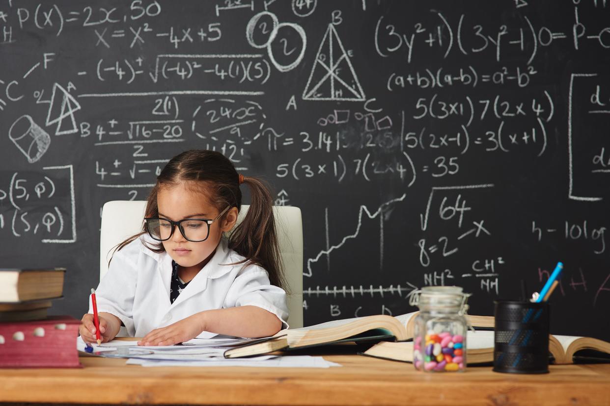 gifted child sitting at desk with math on blackboard