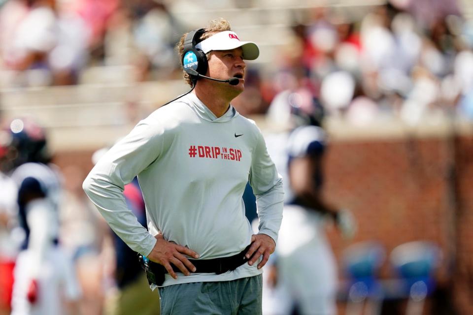 Lane Kiffin stands on the sideline with his hands on his hips.