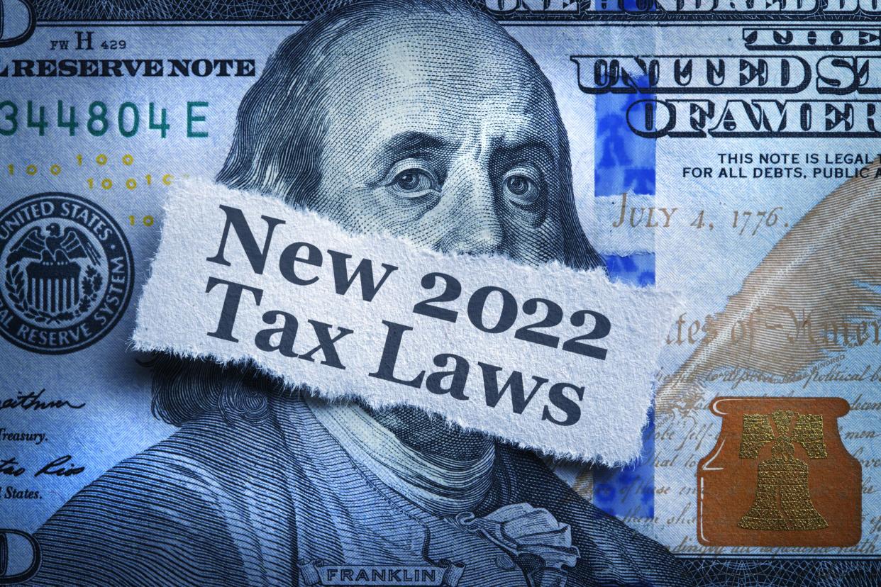 A torn piece of paper telling of the new 2022 tax laws rests on top of a one hundred dollar bill.