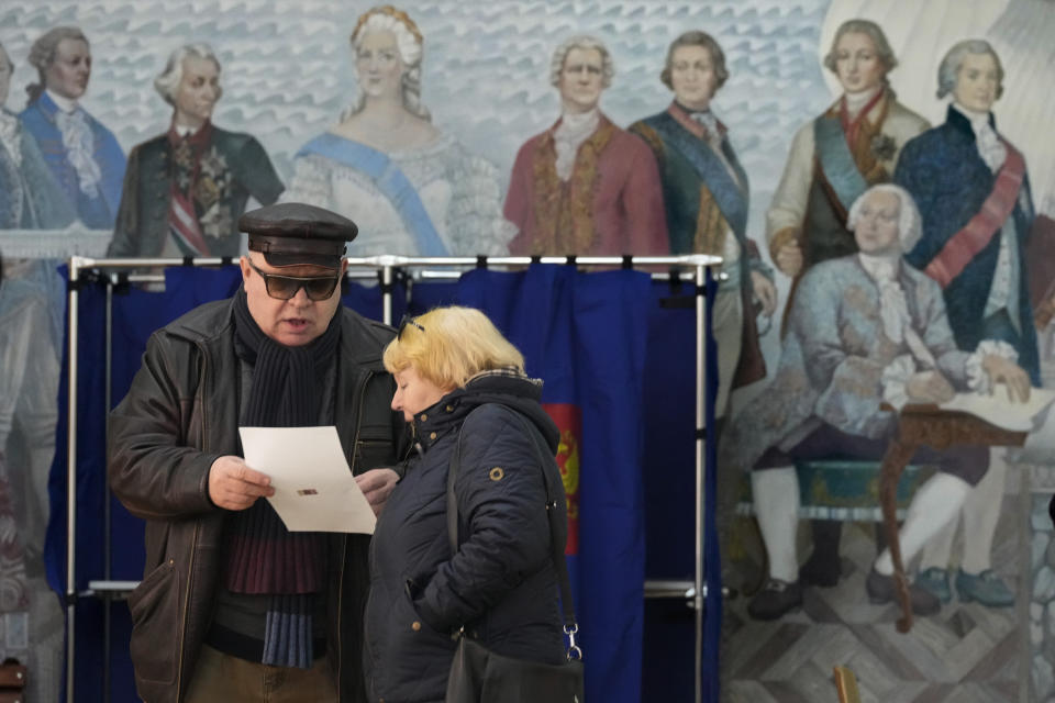 People examine a ballot at a polling station located in a school during the presidential elections in St. Petersburg, Russia, Saturday, March 16, 2024, with a painting depicting the Russian Tsarina Catherine II and her contemporaries on the wall. Voters in Russia are heading to the polls for a presidential election that is all but certain to extend President Vladimir Putin's rule after he clamped down on dissent. (AP Photo/Dmitri Lovetsky)