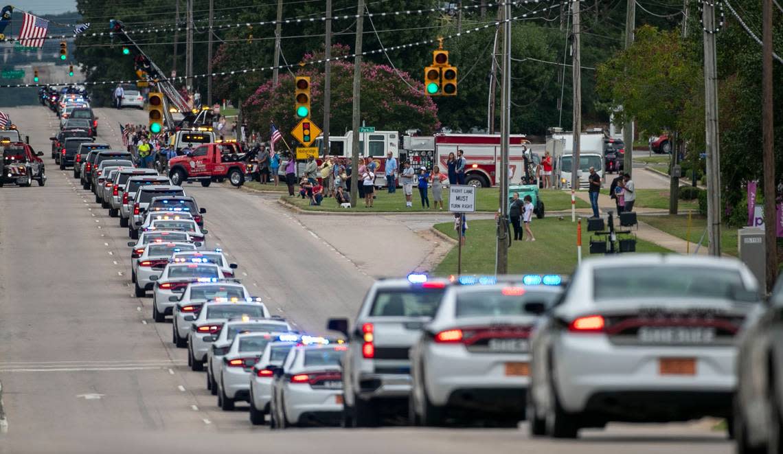 A small group of onlookers gather at the intersection of Glenwood Avenue and Oak Park Road to watch the funeral recessional for Wake County Deputy Ned Byrd after his service at Providence Baptist Church on Friday, August 19, 2022 in Raleigh, N.C.