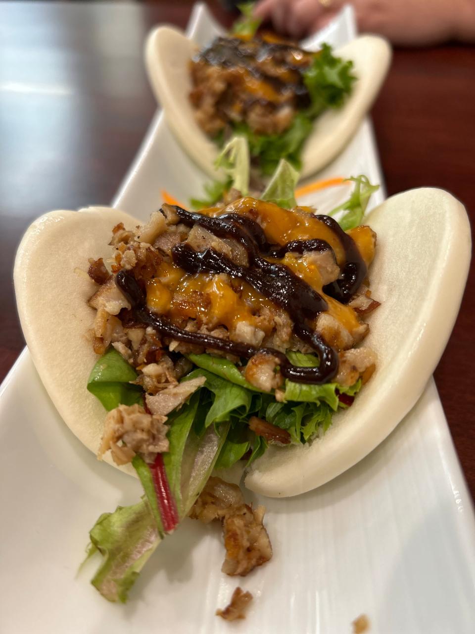 Moo shu pork belly buns are two soft bao buns with pork belly, spring mix greens and spicy mayo.
