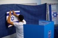 A man hangs up an Israeli flag at a polling station as Israelis begin to vote in a parliamentary election in Rosh Ha'ayin, Israel