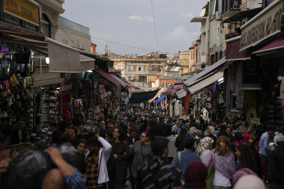 People walk along a commercial street with clothes shops in Istanbul, Turkey, Friday, Oct. 14, 2022. As the value of the U.S. dollar soars, other currencies around the world are sinking by comparison. (AP Photo/Khalil Hamra)