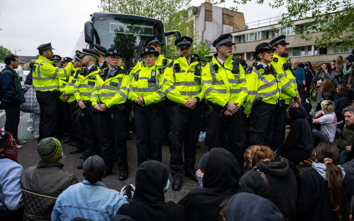 Police officers prepare to move protesters surrounding a bus that was to be used to carry migrants from a hotel