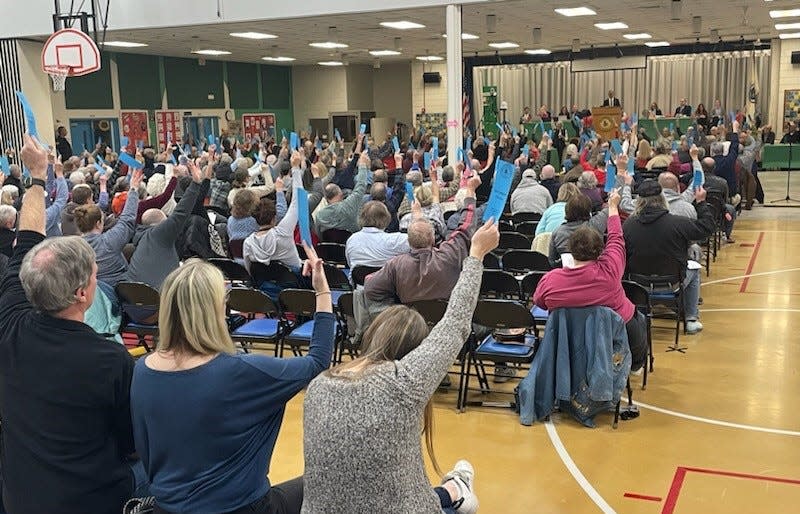 Brewster voters raise their cards on Monday at the town meeting.