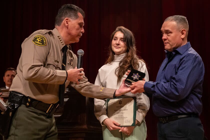 Los Angeles, CA - March 03: Sheriff Robert Luna, left presents a service badge for Alex Martinez to his teary eyed sister Dayanna Martinez and father Arturo Martinez at LA County Sheriff Academy Class 464 graduation ceremony. Alex Martinez is critically injured in an incident about 4 months ago when an SUV veered the wrong way on the road and crashed into Academy Class 464 on a morning exercise jog in Whittier. Graduation ceremony took place at East Los Angeles College on Friday, March 3, 2023 in Los Angeles, CA. (Irfan Khan / Los Angeles Times)