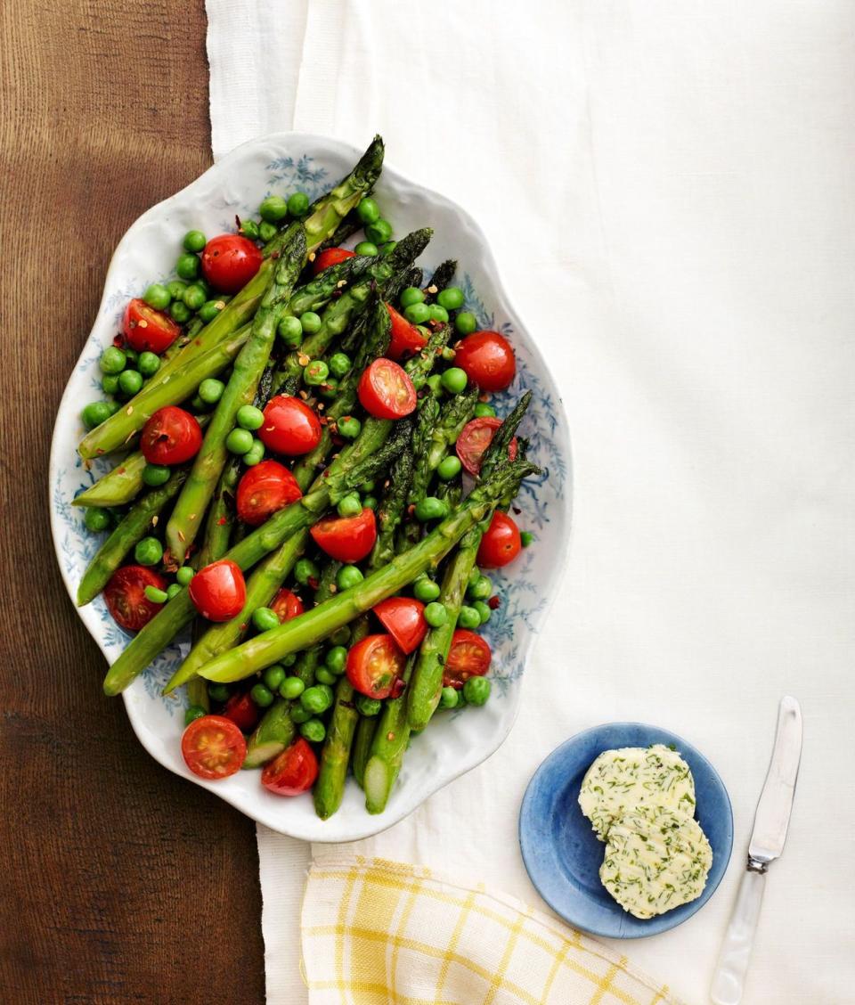 asparagus peas and tomatoes in an antique serving dish with a small blue plate of herb butter on the side