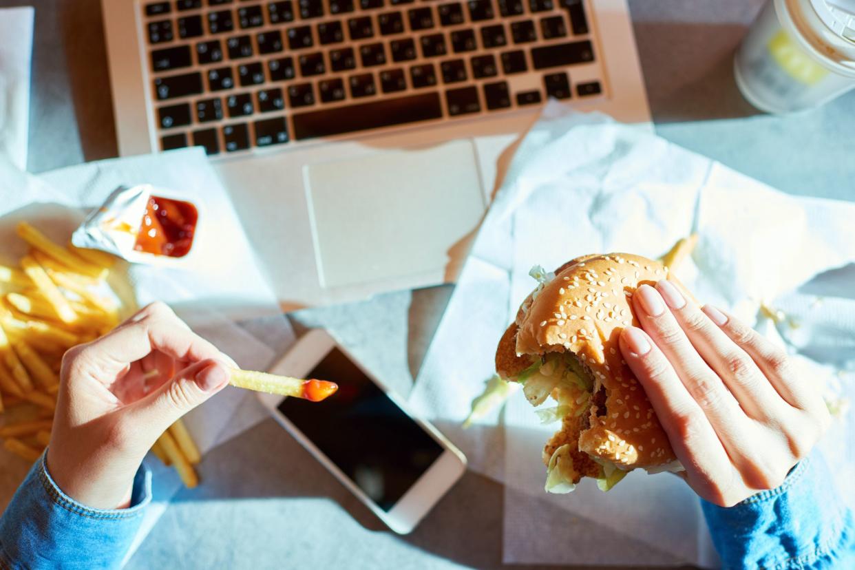 hands holding fries and burger, laptop in background