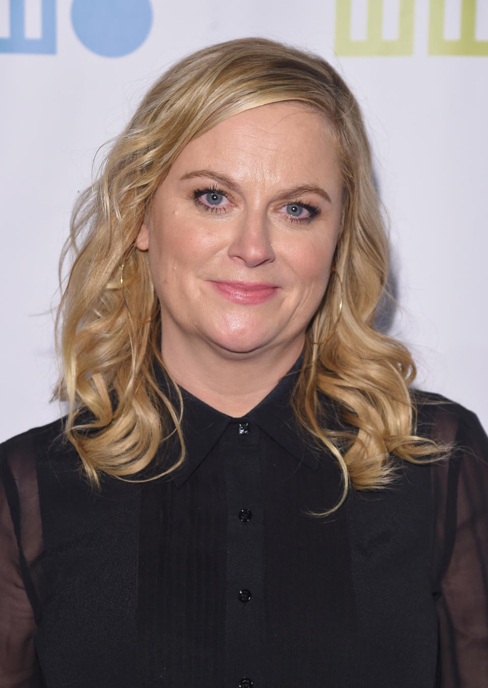 Celebrity at an event in a sheer black top with buttons, smiling for the camera