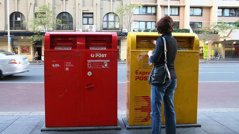 Woman puts letter in Australia Post delivery box. 