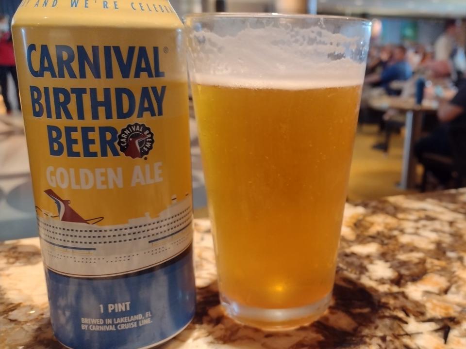 A poured glass of beer with a can next to it that says, "Carnival birthday beer."