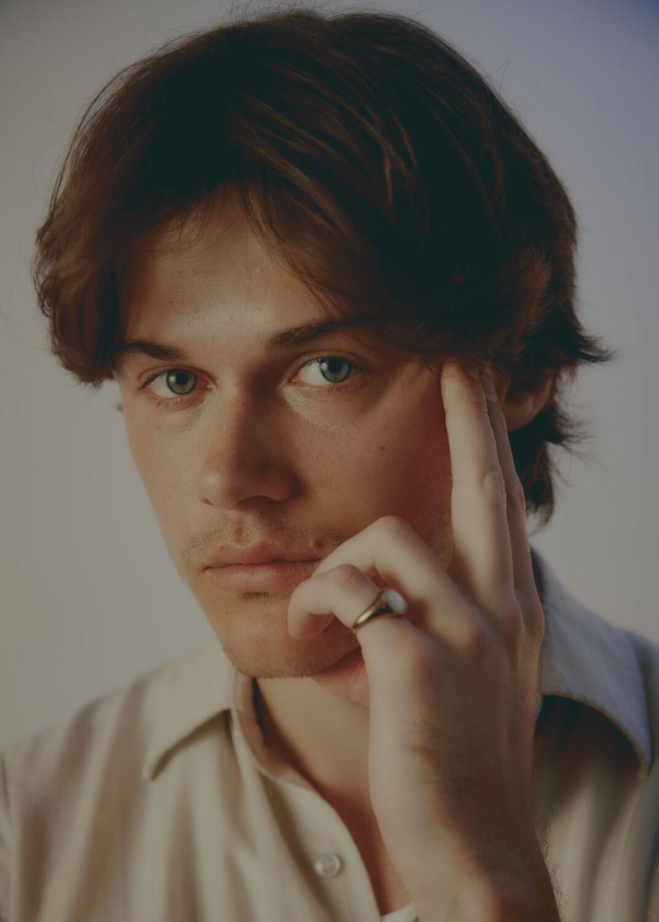 A young man puts his hand to his cheek in a portrait