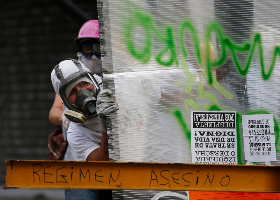 Masked anti-government demonstrators take cover from tear gas fired by Bolivarian National Police using a plastic sheet at a barricade in Caracas, Venezuela, Tuesday, April 1, 2014. Calling them guarimbas, which Venezuelans associate with home base in a child’s game of hide-and-seek, President Nicolas Maduro has repeatedly cited the barricades as evidence that his opponents aren’t fit to govern. (AP Photo/Fernando Llano)