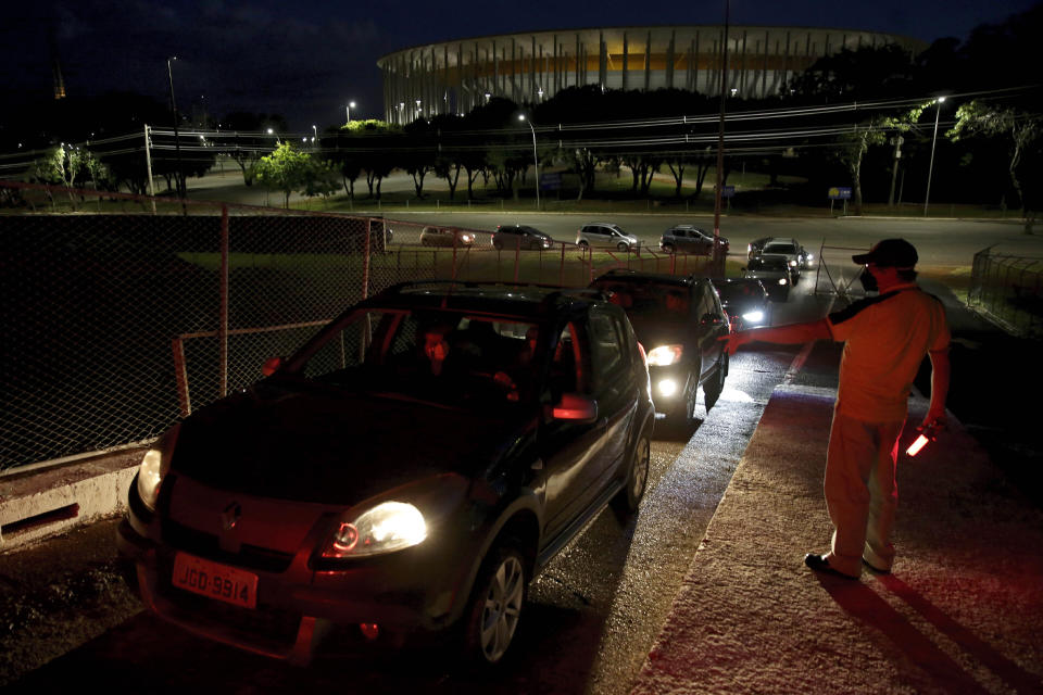 Jair de Souza speaks to drivers arriving at a drive-in movie theater, amid the new coronavirus pandemic in Brasilia, Brazil, Wednesday, May 13, 2020. “Every car must respect the distance, leaving a free parking space between you,” he tells each of them. (AP Photo/Eraldo Peres)