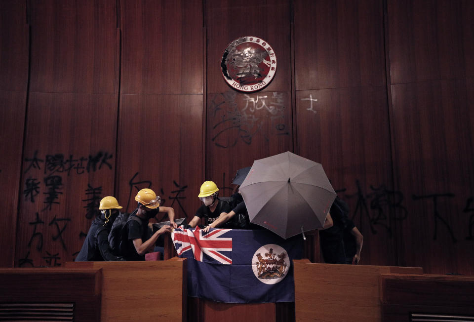 Protesters put a Hong Kong colonial flag and deface the Hong Kong logo at the Legislative Chamber after they broke into the Legislative Council building in Hong Kong, Monday, July 1, 2019. Hundreds of protesters in Hong Kong swarmed into the legislature's main building Monday night, tearing down portraits of legislative leaders and spray-painting pro-democracy slogans on the walls of the main chamber as frustration over a lack of response from the administration to opposition demands boiled over. (AP Photo/Vincent Yu)