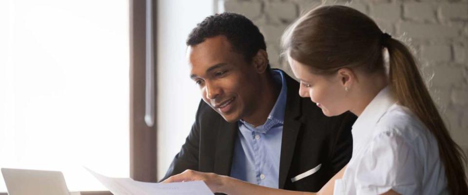 Woman showing man something on a piece of paper while they sit in an office.