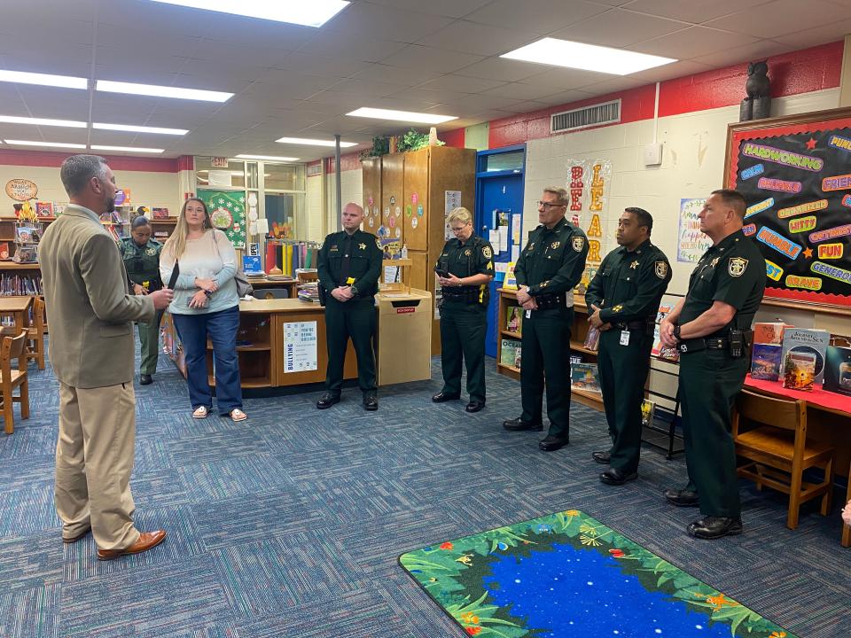 Okaloosa County School District Safe Schools Specialist Danny Dean presents Okaloosa County Sheriff's Office Deputy Jeramy Dobkins (standing in front of desk) with a Certificate of Commendation in front of his supervisors and command staff.