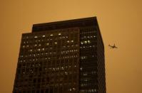 A plane flies past buildings in the Canary Wharf district as the sky turns red as dust from the Sahara carried by storm Ophelia filters sunlight over London, Britain, October 16, 2017. REUTERS/Tom Jacobs