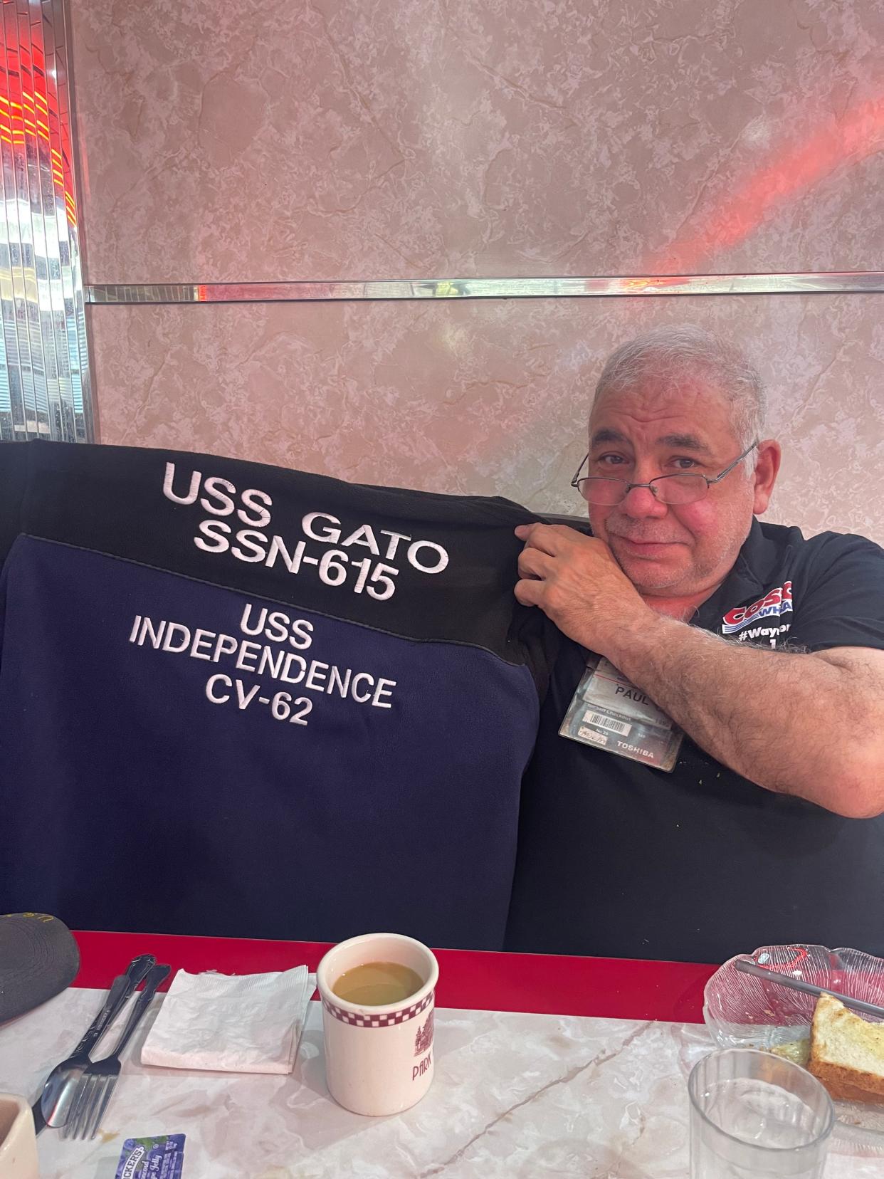 Paul Mistrette at the Clifton Tick Tock Diner talking about his job as a Costco cashier and his love of ballroom dancing. He holds up a jacket with the names of the aircraft carriers he was stationed on during his years in the Navy.