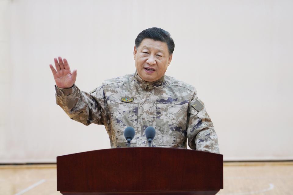 Xi Jinping behind a lectern with an arm raised.