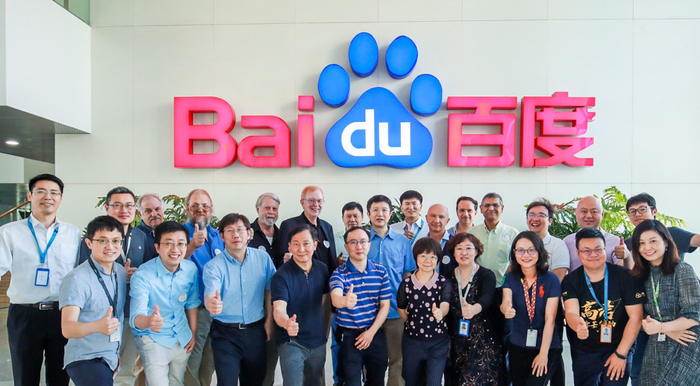 Baidu researchers with their thumbs up in front of Baidu logo.