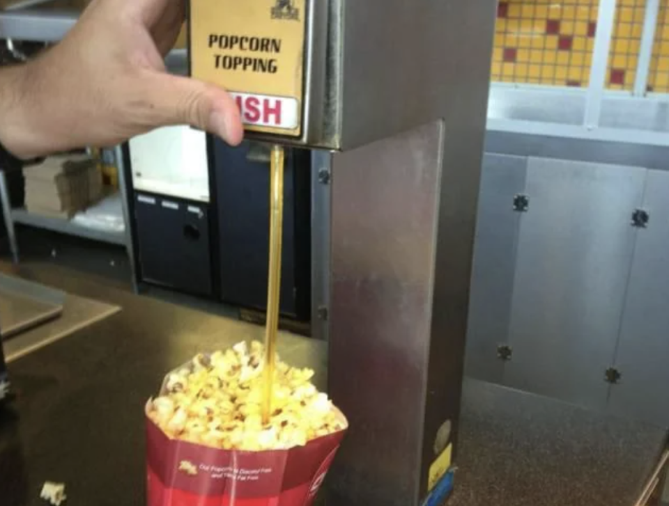 Person pouring liquid butter topping on popcorn at a concession stand