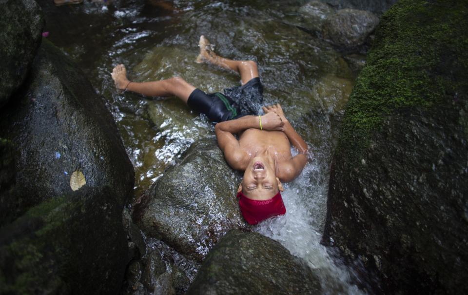 In this photo taken Oct. 12, 2019, a youth lies in water for a cleansing ritual on Sorte Mountain where followers of indigenous goddess Maria Lionza gather annually in Venezuela's Yaracuy state. Believers congregated for rituals on the remote mountainside where adherents make the pilgrimage to pay homage to the goddess, seeking spiritual connection and physical healing. (AP Photo/Ariana Cubillos)