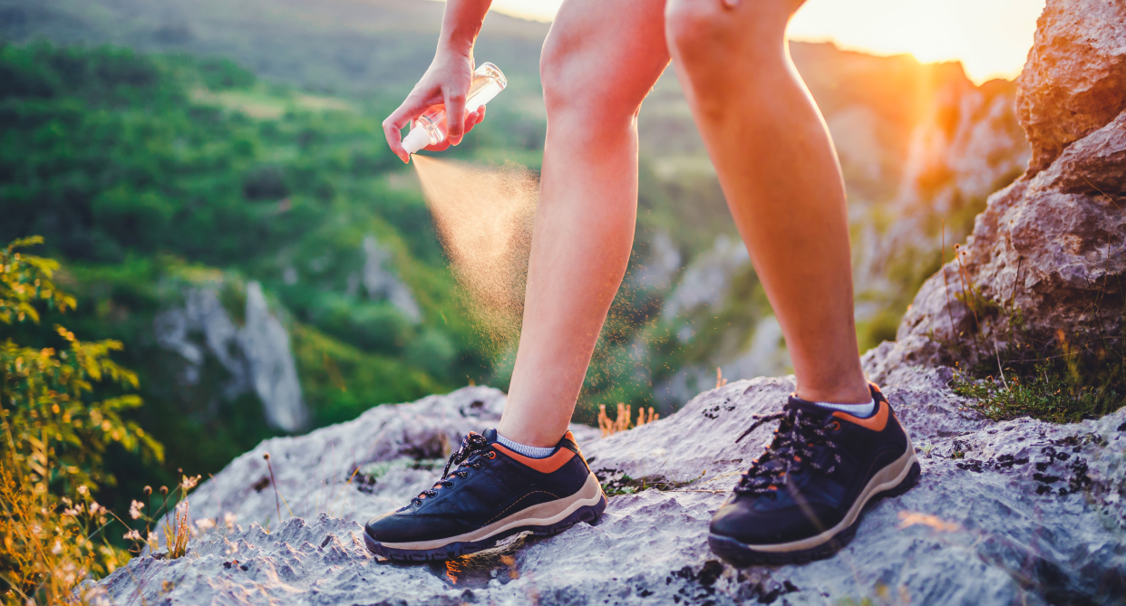 person standing on rock on hike wearing black running shoes spray bug spray on body