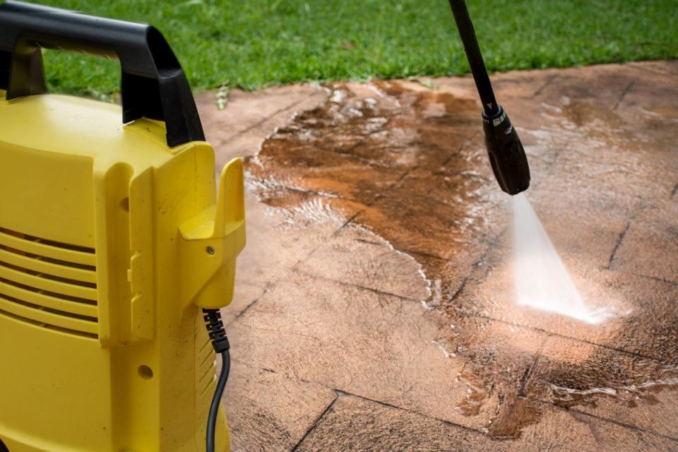 Backyard pavers being cleaned by a yellow pressure washer.