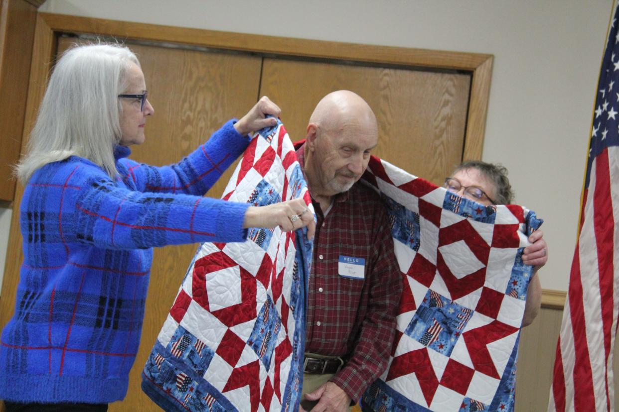 Members of the Perry Piecemakers help wrap Wayne Priest in a Quilt of Valor during a presentation on on Friday, Nov. 10, 2023, at the Perry Elks Lodge.