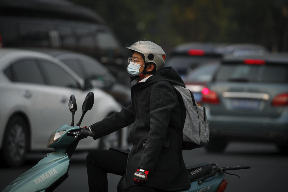 A man wearing a face mask to help curb the spread of the coronavirus rides on a scooter as he waits to cross a street during the morning rush hour in Beijing, Monday, Oct. 26, 2020. Schools and kindergartens have been suspended and communities are on lockdown in Kashgar, a city in China's northwest Xinjiang region, after more than 130 asymptomatic cases of the coronavirus were discovered. (AP Photo/Andy Wong)