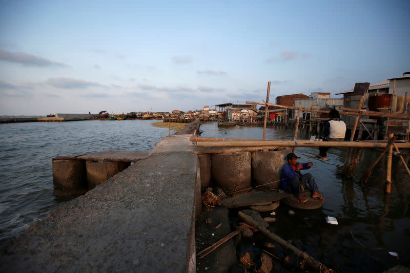 Eko Yuliono, a 45-year-old food vendor, sits on sea wall as he prepares to fish in Tambaklorok village in Semarang